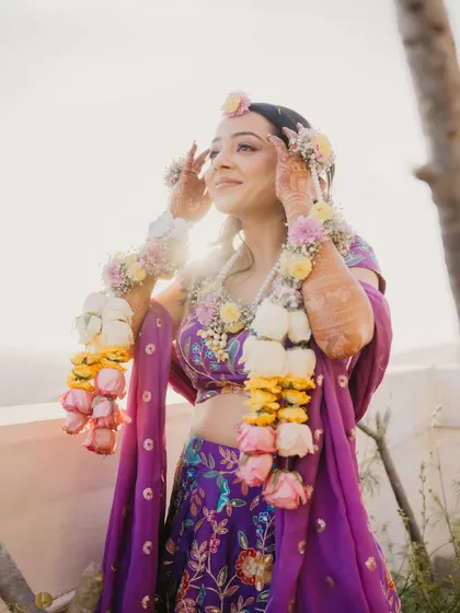 A radiant portrait of the bride adorned with floral jewelry for her haldi ceremony. The golden hour light makes her glow, capturing a moment of serene beauty.