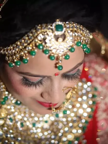 A close-up shot capturing the delicate details of a bride's makeup and jewelry. We focus on capturing the fine craftsmanship of the kundan and emerald jewelry and the bride's serene expression.