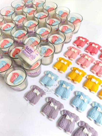 A vibrant collection of baby onesie shaped soy wax sachets and baby feet votive candles, showing the variety of colors and designs available for baby-related events.