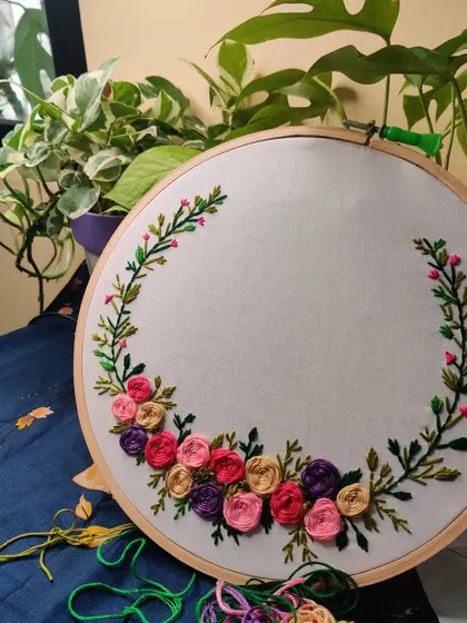 The beginning of a floral wreath embroidery project. This shows the initial flowers stitched, with the threads ready for the next part of the design.
