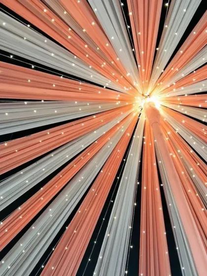 A close-up of a ceiling drape design in peach and white, with fairy lights woven in. This technique creates a beautiful radiating pattern of light and color.