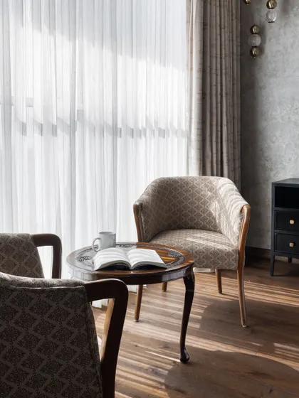 We designed this quiet reading corner with earthy tones and natural light in mind. The classic armchairs and carved wooden table create a perfect spot to relax with a book and a cup of coffee.
