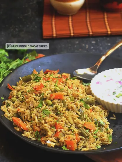 A plate of our flavorful Vegetable Pulao, cooked with long-grain rice, mixed vegetables, and aromatic spices, served with a side of cooling raita.