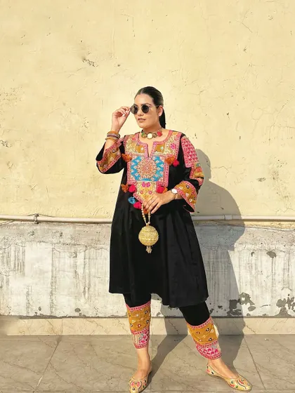 This black kurta set with vibrant, multi-colored Afghan-style embroidery is a bold and beautiful statement. It's paired with a golden potli bag for a complete festive look.