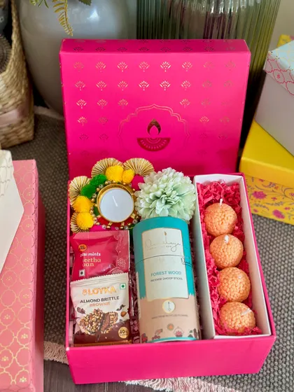 A vibrant pink Diwali box, perfect for gifting. It includes a set of 4 ladoo candles, dhoop sticks, and almond brittle.