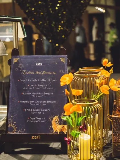 An elegant menu for "India's Test Flavours" biryani station, set against golden decor.