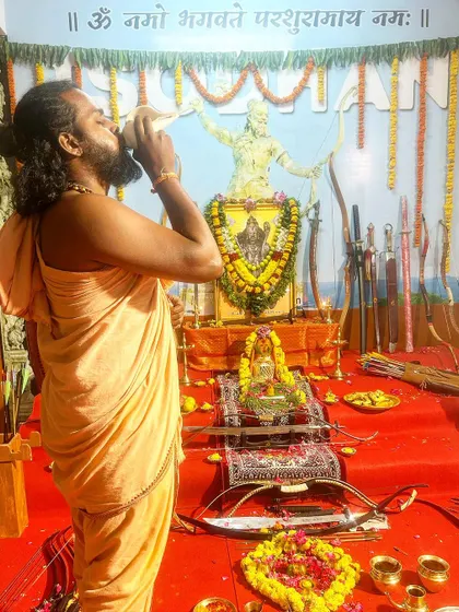 I begin the Ayudha Puja by blowing the conch shell, a sacred sound that purifies the atmosphere and signals the start of the auspicious ceremony to honor our weapons.