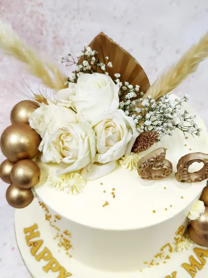 We celebrate a 60th birthday in style with this chic white and gold floral cake. Fresh white roses and dried pampas grass create a modern botanical arrangement, while gold spheres and lettering add a touch of luxury to the pristine ivory cake.