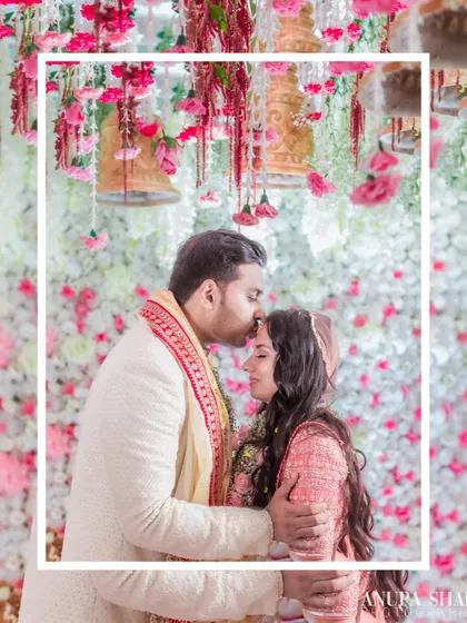 A tender moment under a canopy of flowers. The groom kisses the bride's forehead, a classic, heartfelt gesture of love and protection.