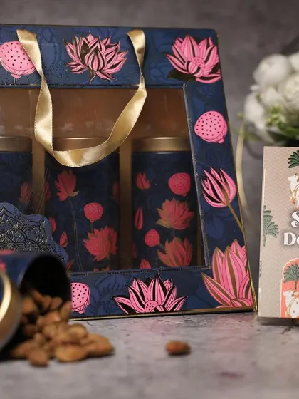 A beautiful navy blue and pink lotus-themed dry fruit box. The window allows a peek at the goodies inside, and the design is quintessentially festive.