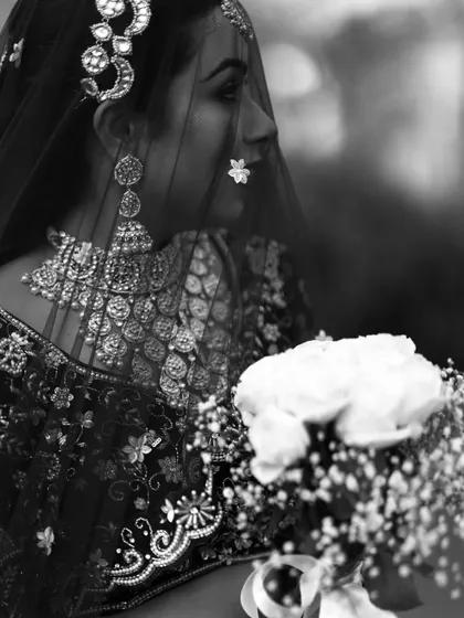 A beautiful black and white profile of the bride, her face partially covered by her veil, holding a bouquet of white roses.
