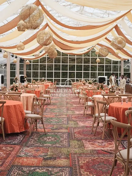 The dining area for the Souk-themed Mehendi, featuring a floor covered in printed carpets, rustic wooden chairs, and a ceiling of flowing earthy-toned drapes.