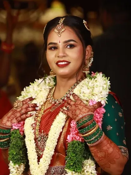 A happy bride, her hands framing her necklace, giving a great view of her intricate mehendi.