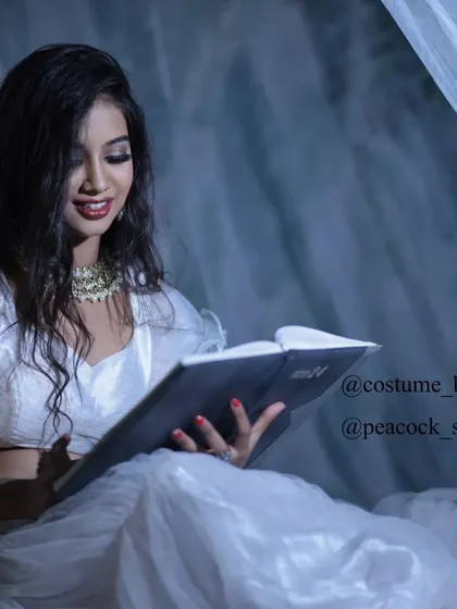 A whimsical shot of a model in a white outfit, reading a book in a softly lit, dreamy setting.