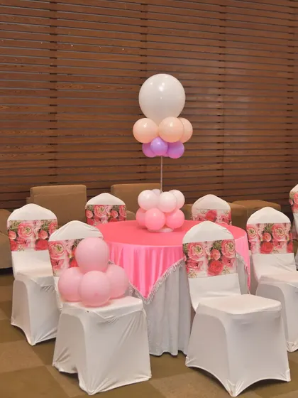 I also provide decorations for guest seating areas. This setup includes a balloon centerpiece for the table and custom-printed floral chair covers to match the event's theme.