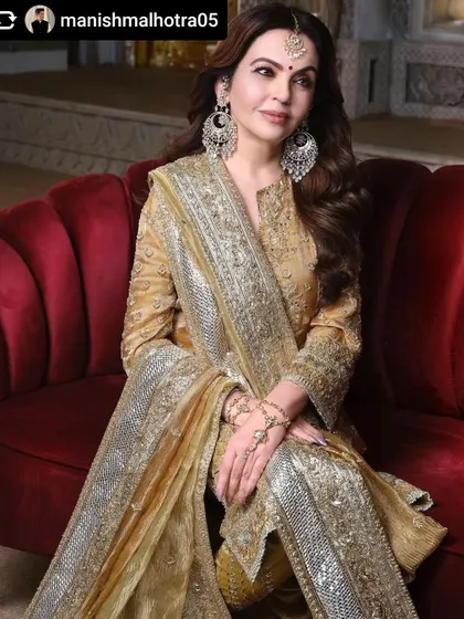 A beautiful and graceful portrait of Mrs. Nita Mukesh Ambani. The rich red of the sofa provides a wonderful contrast to her golden attire, creating a regal and sophisticated image.
