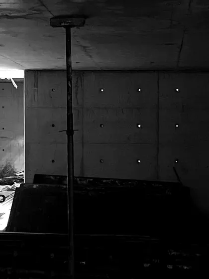 A dark, atmospheric shot of an unfinished basement space. Small points of light penetrate the concrete wall, which are tie-rod holes left over from the formwork.