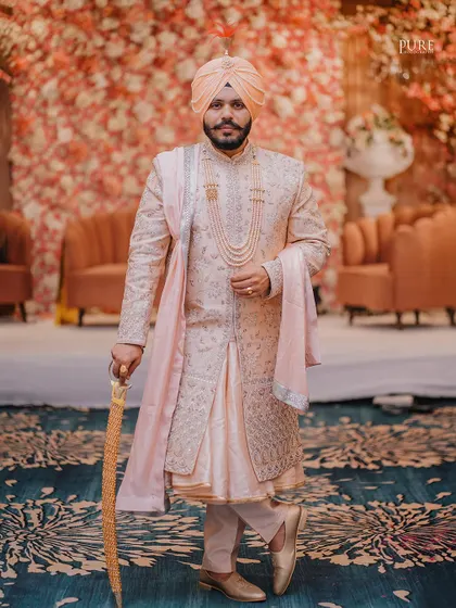 A full-length portrait of the groom on his wedding day. His royal posture, traditional sherwani, and kirpan create a powerful and elegant image.