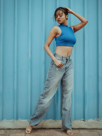 A modern portfolio shot with a clean, vibrant aesthetic. The bold blue background contrasts with the casual denim and crop top, creating a striking image perfect for a model's lookbook or a contemporary personal portrait.