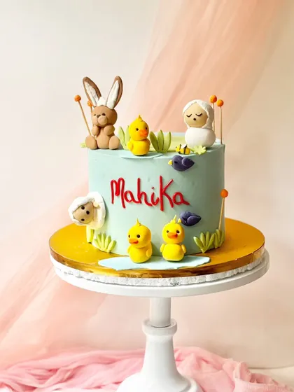 A sweet spring-themed cake with little fondant animals. It features a bunny, ducklings, and a lamb, perfect for an Easter celebration or a first birthday.