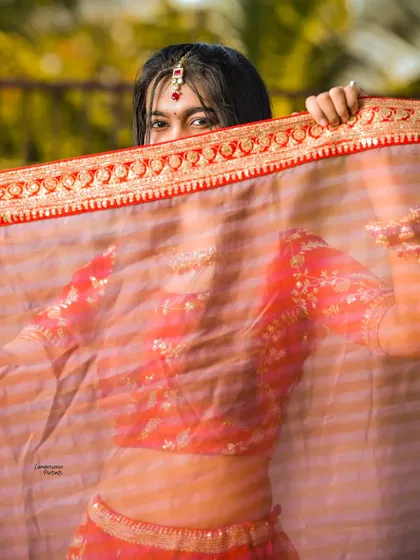 A peek-a-boo shot of the bride, her eyes playfully visible through her sheer red dupatta, adding a touch of mystery and fun.