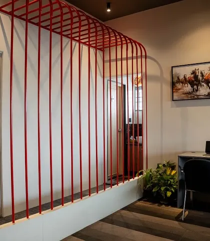 This open workstation is defined by a minimalist red metal frame, which acts as a light and airy space divider. It's a simple yet effective way to create zones in an open-plan office.