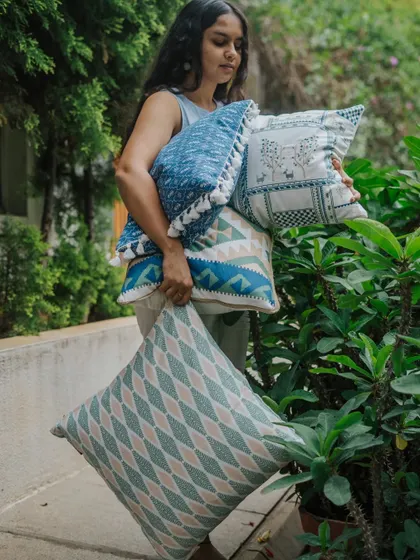 Our designer carrying a stack of blue-themed cushion covers, showcasing the variety of prints, textures, and details available in our collection.
