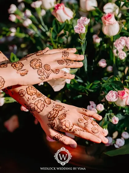 The beauty of Mehendi is in the details. This intricate floral henna design is perfectly complemented by a backdrop of fresh pink and white roses, showcasing a blend of tradition and artistry.