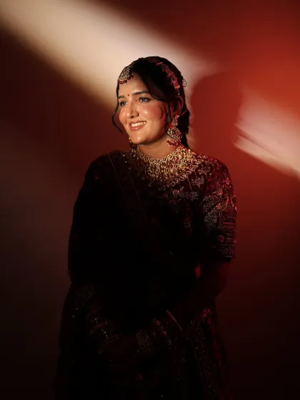 Another beautiful portrait of the smiling bride. This image clearly shows the defined yet natural eye makeup and the perfect shade of lipstick chosen to match her royal velvet lehenga.