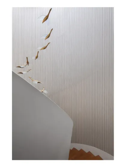 A detail of the custom art installation, where bird-like forms ascend along the fluted wall of the staircase, adding a sense of movement and poetry.