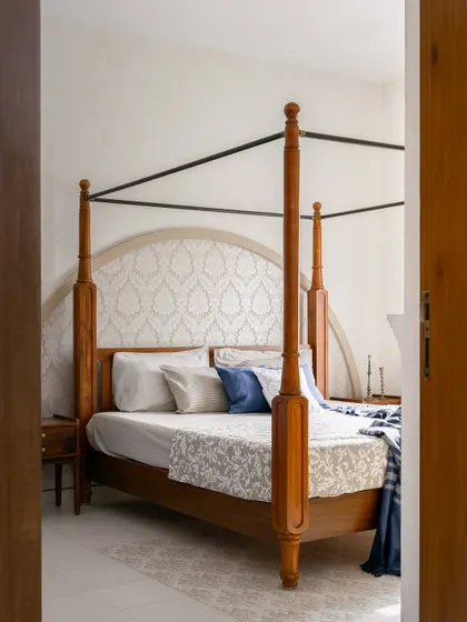 A view into the bedroom, where a classic four-poster bed with an arched, patterned headboard creates an elegant and serene focal point.