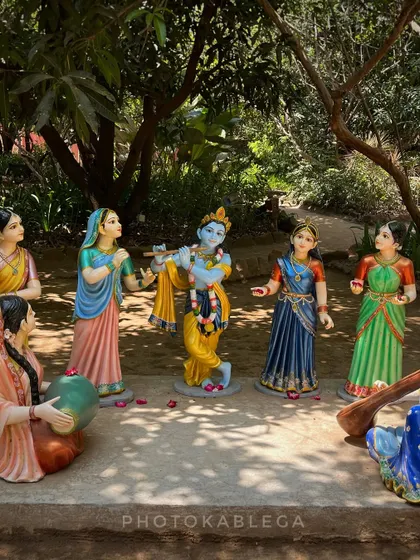 A vibrant statue display of Krishna playing his flute, surrounded by the gopis in a forest-like setting.