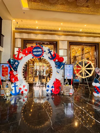 The grand entrance for a nautical "Welcome Aboard" party, with a circular arch decorated with anchors, a ship's wheel, and red, white, and blue balloons.