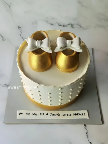 Happy Mother's Day! A beautiful baby shower cake with golden baby booties and a delicate white bow. A perfect way to celebrate a mom-to-be.