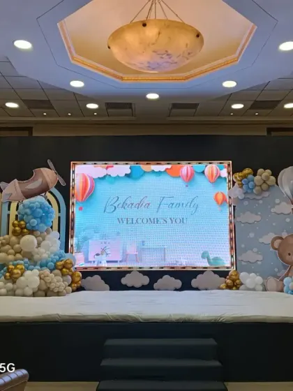 A grand stage setup featuring a hot air balloon and airplane theme. This design is perfect for a large baby shower or welcome party in a banquet hall, complete with a digital screen for custom messages and adorable teddy bear props.