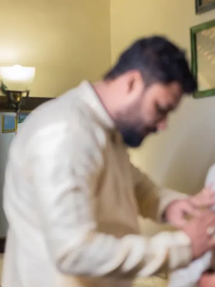 A candid, behind-the-scenes moment of the groom getting help with his outfit before the ceremony.