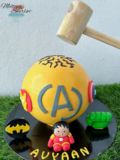 Get ready to smash! This is our super popular superhero pinata cake. The yellow chocolate sphere is decorated with Avengers and Batman logos and comes with a hammer to crack it open, revealing a fun surprise of candies inside.