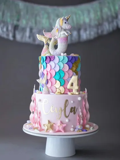 A whimsical unicorn-mermaid, or "mer-corn," cake for a 4th birthday. This creative two-tiered cake combines two popular themes with colorful scales and a magical topper.