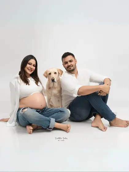 A beautiful family-of-three portrait, with the expecting couple and their dog sitting together, looking confidently at the camera.