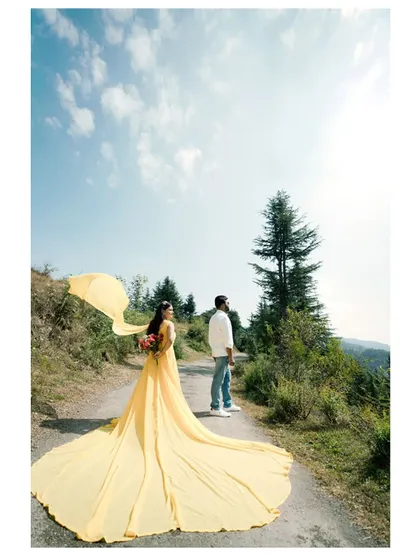 A "follow me" style shot on a mountain path. The bride's vibrant yellow dress contrasts beautifully with the green landscape, and the flowing train adds a sense of movement.