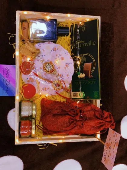 An overhead view of a complete Rakhi hamper. This set includes a rakhi, perfume, dark chocolate, and other traditional elements, making it a perfect package to send your love.