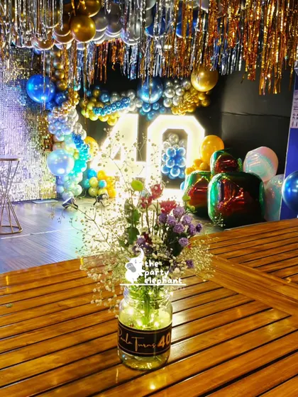 Even the table centerpieces were part of the theme. This simple yet elegant arrangement features wildflowers in a jar with a custom 'Paula Turns 40' label, with the dazzling party decor in the background.