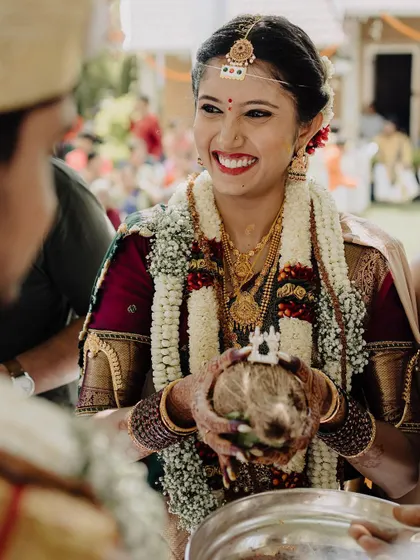 A bride’s radiant smile during a traditional ceremony, holding the sacred coconut. The warm, natural light highlights her joy and the rich details of her attire, a perfect example of candid wedding photography.