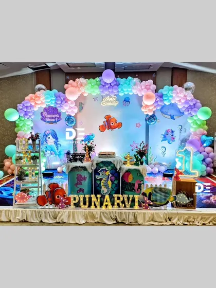 An enchanting underwater mermaid theme for Punarvi's first birthday. This grand setup includes characters from 'Finding Nemo', mermaid cutouts, and a stunning balloon arch that mimics ocean waves.