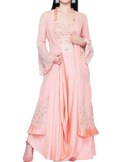 An elegant peach-colored indo-western set featuring dhoti-style pants, an embroidered bustier, and a matching longline jacket with bell sleeves. This is a high-fashion choice for a stylish wedding guest.