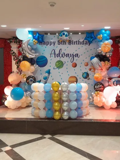 An out-of-this-world Space-themed stage setup for Advaya's 5th birthday. The backdrop features planets and stars, framed by a stunning balloon arrangement with astronaut and rocket foils.