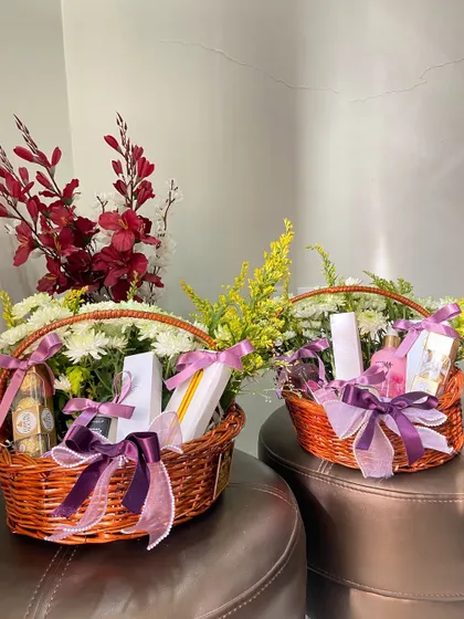 Two beautiful floral gift baskets ready for a celebration. Filled with flowers and goodies and tied with purple ribbons, they are perfect for birthdays, anniversaries, or as thank you gifts.