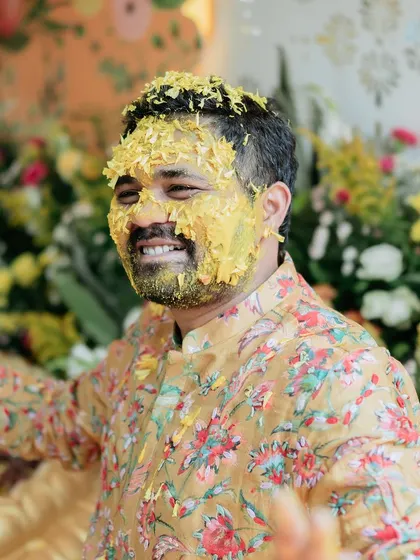 The groom, covered in turmeric paste, flashes a joyful smile, fully enjoying the fun and traditions of his Haldi ceremony.