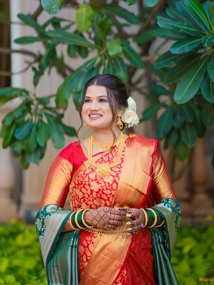 A beautiful outdoor portrait of a bride in her traditional red and green wedding saree, smiling happily.