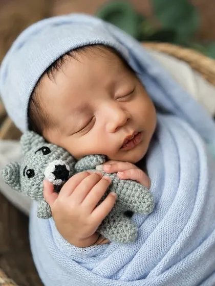 This little one looks just like a doll, cuddling a tiny grey teddy bear. The soft, light blue wrap and sleepy hat create a dreamy and gentle portrait.